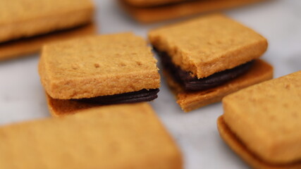 A close-up of handmade chocolate sandwich cookies tied with rustic twine, neatly stacked on a wooden plate. The golden brown biscuits with rich chocolate filling evoke a warm, homemade feel. Styled in