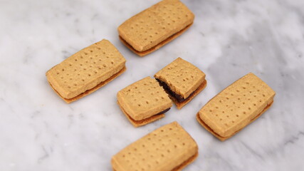 A close-up of handmade chocolate sandwich cookies tied with rustic twine, neatly stacked on a wooden plate. The golden brown biscuits with rich chocolate filling evoke a warm, homemade feel. Styled in