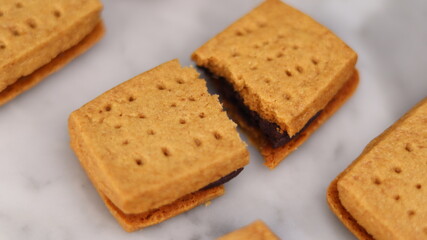 A close-up of handmade chocolate sandwich cookies tied with rustic twine, neatly stacked on a wooden plate. The golden brown biscuits with rich chocolate filling evoke a warm, homemade feel. Styled in