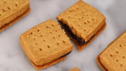 A close-up of handmade chocolate sandwich cookies tied with rustic twine, neatly stacked on a wooden plate. The golden brown biscuits with rich chocolate filling evoke a warm, homemade feel. Styled in