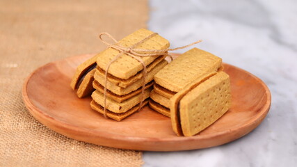 A close-up of handmade chocolate sandwich cookies tied with rustic twine, neatly stacked on a wooden plate. The golden brown biscuits with rich chocolate filling evoke a warm, homemade feel. Styled in