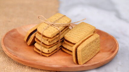 A close-up of handmade chocolate sandwich cookies tied with rustic twine, neatly stacked on a wooden plate. The golden brown biscuits with rich chocolate filling evoke a warm, homemade feel. Styled in
