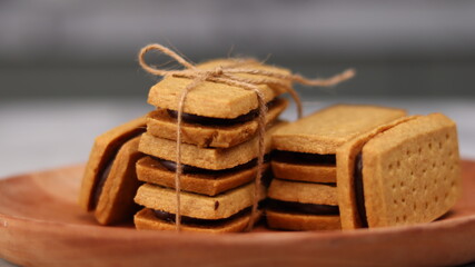 A close-up of handmade chocolate sandwich cookies tied with rustic twine, neatly stacked on a wooden plate. The golden brown biscuits with rich chocolate filling evoke a warm, homemade feel. Styled in