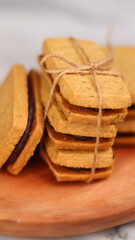 A close-up of handmade chocolate sandwich cookies tied with rustic twine, neatly stacked on a wooden plate. The golden brown biscuits with rich chocolate filling evoke a warm, homemade feel. Styled in