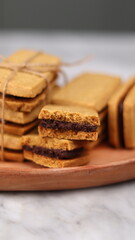 A close-up of handmade chocolate sandwich cookies tied with rustic twine, neatly stacked on a wooden plate. The golden brown biscuits with rich chocolate filling evoke a warm, homemade feel. Styled in