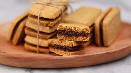 A close-up of handmade chocolate sandwich cookies tied with rustic twine, neatly stacked on a wooden plate. The golden brown biscuits with rich chocolate filling evoke a warm, homemade feel. Styled in