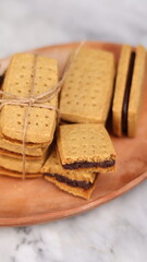 A close-up of handmade chocolate sandwich cookies tied with rustic twine, neatly stacked on a wooden plate. The golden brown biscuits with rich chocolate filling evoke a warm, homemade feel. Styled in