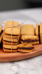 A close-up of handmade chocolate sandwich cookies tied with rustic twine, neatly stacked on a wooden plate. The golden brown biscuits with rich chocolate filling evoke a warm, homemade feel. Styled in