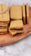 A close-up of handmade chocolate sandwich cookies tied with rustic twine, neatly stacked on a wooden plate. The golden brown biscuits with rich chocolate filling evoke a warm, homemade feel. Styled in