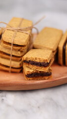 A close-up of handmade chocolate sandwich cookies tied with rustic twine, neatly stacked on a wooden plate. The golden brown biscuits with rich chocolate filling evoke a warm, homemade feel. Styled in