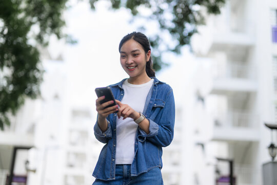 Happy asian woman using mobile phone while walking in urban city background