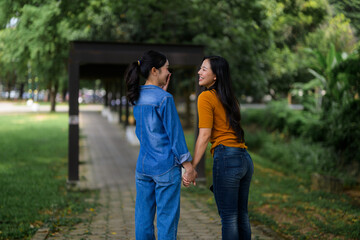 Two friends enjoying a leisurely stroll, holding hands and chatting happily in a green park