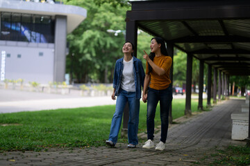 Two friends enjoying a leisurely stroll in a park, sharing laughter and pointing at something interesting