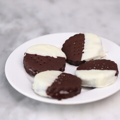 Delicious homemade chocolate ice cream sandwich cookies half dipped in white chocolate, served on a white plate over a marble background. A perfect frozen dessert or sweet treat for summer