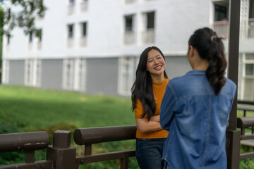 Two young women chatting and smiling near a railing in a university campus