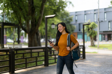 Young Asian student walking in a park using her smartphone