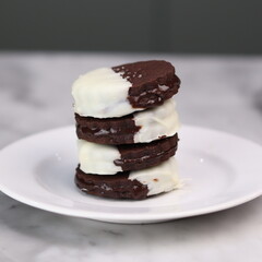 Delicious homemade chocolate ice cream sandwich cookies half dipped in white chocolate, served on a white plate over a marble background. A perfect frozen dessert or sweet treat for summer