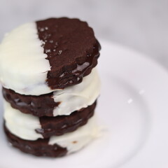 Delicious homemade chocolate ice cream sandwich cookies half dipped in white chocolate, served on a white plate over a marble background. A perfect frozen dessert or sweet treat for summer