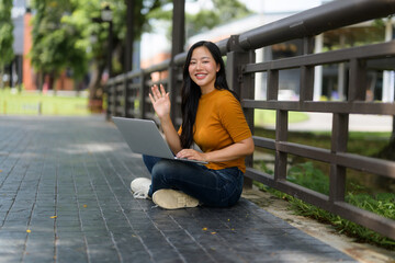 Freelancer working remotely having a video conference in a park, waving at the laptop screen