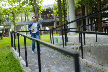 Asian female college student going up an accessible ramp in a university campus, holding a laptop, and smiling
