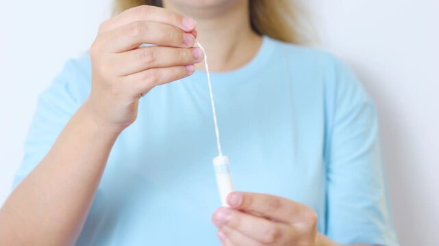 Woman grasping feminine hygiene product tampon by string, representing menstrual wellness, personal care, and monthly cycle management with confident, natural approach