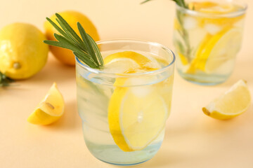 Glasses of fresh lemonade with rosemary and lemons on beige background, closeup