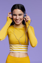sport fitness woman smiling and enjoying music wearing yellow activewear with headphones against purple background, healthy lifestyle, workout motivation