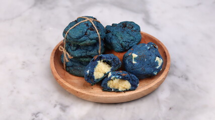 Vibrant blue chocolate chip cookies stacked and bundled with twine, served on a round wooden plate over a marble background. Eye-catching artisanal cookies perfect for bakery showcases, creative desse