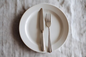 A minimalist dining setup featuring a white ceramic plate with a silver knife and fork placed on a light-colored linen tablecloth