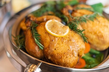 Roasted chicken with lemon and herbs on a platter. Juicy chicken, garnished with rosemary and lemon slices. Perfectly cooked chicken, ready to serve. Sunday roast, roasted chicken with rosemary.