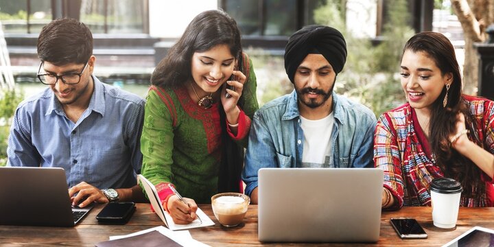 Indian group of friends collaborating and brainstorming at a table with laptops. They engage in teamwork, sharing ideas and working together effectively.