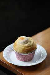 Coconut-filled bun in a pink cupcake wrapper on a white plate, placed on a wooden table with dark background. Ideal for bakery, sweet pastry, or cafe menu design.