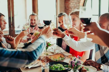 Group of people toasting with wine glasses at a dining table. Celebration, diverse group, enjoying a meal together, cheerful atmosphere, festive gathering. Celebrations, Communal dining.