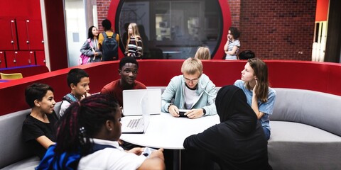 Diverse group of students sitting around a table, engaged in discussion. Mixed ethnicities, both...