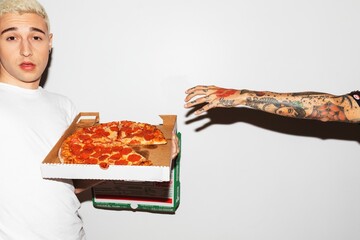 A person holding a pizza box with pepperoni pizza. Another tattooed arm reaches for a slice. Pizza, tattoos, and reaching hands in a casual setting. Man grabbing a pizza slice from a friend.