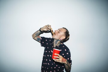Tattooed person enjoying food, holding a red cup. Tattoos, red cup, and food highlight the scene....