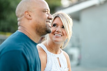 Obraz premium A man and woman smiling outdoors. The woman looks at the man with a smile. Couple are enjoying together in a relaxed setting. Relaxed couple standing outdoor enjoying together.