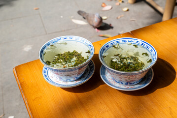 Two bowls of green tea on a wooden table with a pigeon in the ba