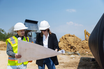 Two construction professionals examine site blueprints at an active urban construction area, with a...