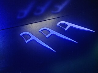 Three dental floss tools aligned in a row, captured under blue lighting to highlight their modern...