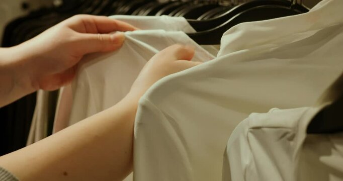 Woman examining white shirt, checking price tag while browsing clothing store, evaluating garment quality and affordability