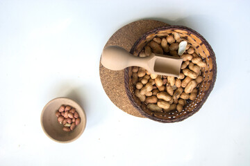 Peanuts in a basket with a wooden scoop on a white background