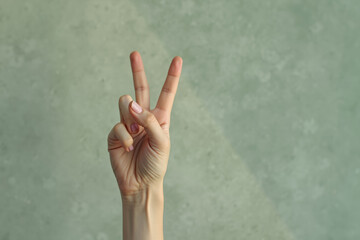 hand displays a peace sign with two fingers raised against a muted green background.