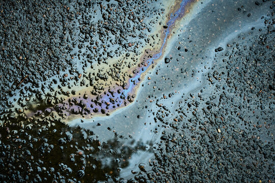 Gasoline or oil spill polluting water on asphalt road surface creating rainbow sheen. - Powered by Adobe