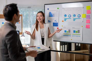 A woman is standing in front of a white board with a man standing behind her