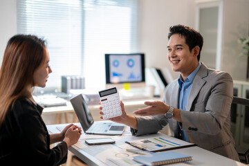 A man and a woman are sitting at a desk with a calculator in front of them