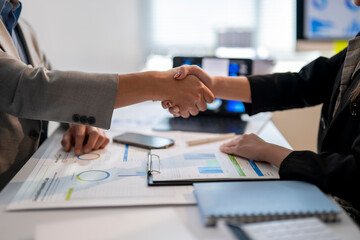 Two people shaking hands in front of a table with papers and a laptop