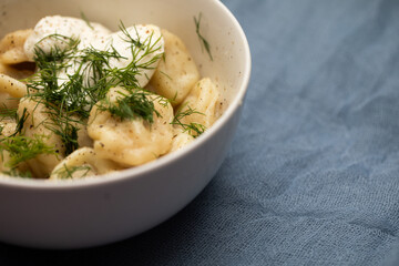a closeup of delicious bowl of pelmeni with dill and sour cream on blue cloth