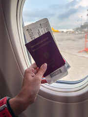Holding a passport and boarding pass by the window on a flight