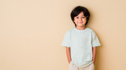Obraz premium A happy young boy is posing against a beige backdrop. His cheerful expression and casual pose convey a sense of joy and innocence.